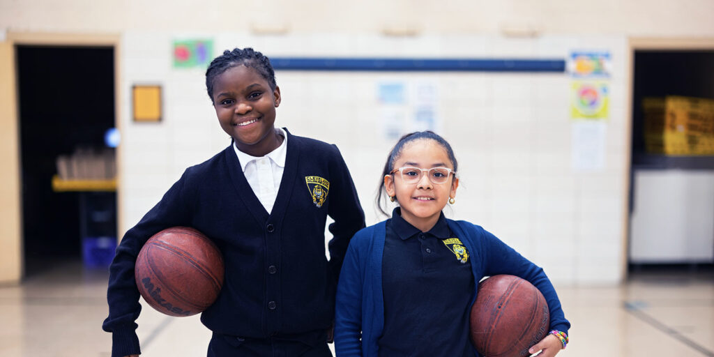 Smiling students holding basketballs in the gym.